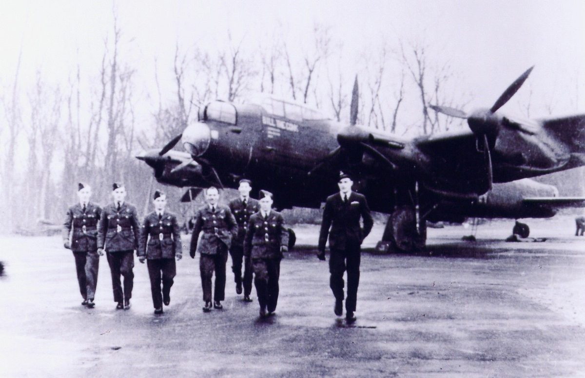 Bill Woods and his Lancaster bomber crew walking across the airfield, their aircraft visible behind them